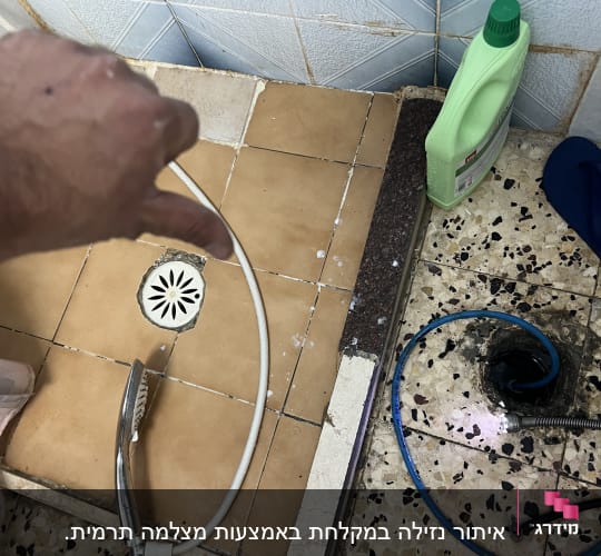 יד מצביעה על רצפה עם צינור ומכשיר ניקוז